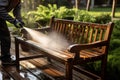 Focused cleaning person pressure washes garden furniture bench under the sun