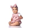 Focused concentrated infant baby girl toddler in polka-dot dress and headband with bow sits on the white floor