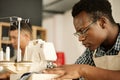 Focused designer sewing fabric. Focused tailor using sewing machine. African American designer sewing a piece of denim Royalty Free Stock Photo