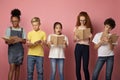 Focused diverse schoolkids reading books over pink background