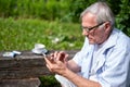 Focused elder with trendy glasses taps on a phone, blending tradition with technology in a bright outdoor setting, and Royalty Free Stock Photo