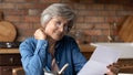 Focused elderly latin woman engaged in reading letter from bank