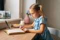 Focused elementary child school girl writing to notebook with pen looking on paper book. Homeschooling concept. Royalty Free Stock Photo