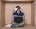 Focused employee wearing VR glasses sits in his cardboard office