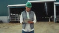 Focused engineer making notes at modern cowshed building in protective helmet.