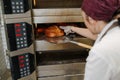 Focused female baker taking bread from oven furnace with special flat showel Royalty Free Stock Photo