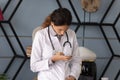 Focused female doctor in white texting on smartphone