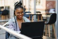 Focused female office worker using computer in coffee shop. African American business woman working on laptop in cafe and looking Royalty Free Stock Photo