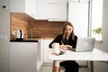 focused female student studies at home, sitting in kitchen with laptop and writing notes in notebook. online learning, self-study Royalty Free Stock Photo