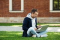 Focused freelancer man sitting on grass with legs crossed remote work on laptop, using smartphone. Royalty Free Stock Photo