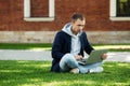 Focused freelancer man sitting on grass in park with legs crossed remote work on laptop outdoors. Royalty Free Stock Photo