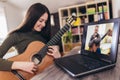 Girl playing acoustic guitar and watching online course on laptop while practicing at home. Online training, online Royalty Free Stock Photo