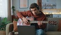 Focused guitarist learning online by laptop video course at apartment couch. Royalty Free Stock Photo