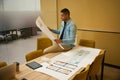 Focused guy sitting on table and holding unrolled plan Royalty Free Stock Photo