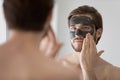 Focused handsome metrosexual guy applying dark cleansing natural clay