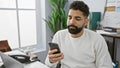 Focused hispanic man using smartphone in a modern office setting, portraying connectivity and work-life integration Royalty Free Stock Photo