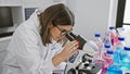A focused hispanic woman scientist examines samples under a microscope in a well-equipped laboratory Royalty Free Stock Photo