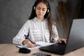 Focused hispanic woman wearing headphones using laptop at home, writing notes, female college student learning and Royalty Free Stock Photo