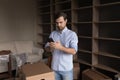 Focused home owner man using smartphone among cardboard boxes