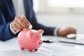 Focused image of a businessman& x27;s hand depositing a coin into a pink piggy bank