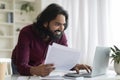 Focused indian man analyzing documents and working on his laptop at home Royalty Free Stock Photo