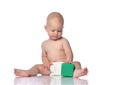 Infant child baby boy in diaper is sitting on the floor looking on a green cube in front of him, playing, touching