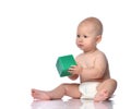 Quiet infant child baby boy in diaper is sitting on the floor with a green cube, playing, giving, taking on white