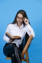 Focused, beautiful lady wearing eyeglasses, reading book, while resting on chair in studio. Royalty Free Stock Photo