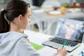 Focused latin teenage girl writing in her copybook while having online lesson, using laptop, sitting at the table at