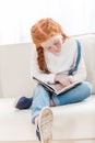 Focused little girl reading book while sitting on sofa at home Royalty Free Stock Photo