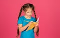 Focused little girl writing in notebook while standing on pink background