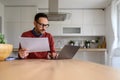 Focused male adviser holding financial reports and working online over laptop at desk in home office Royalty Free Stock Photo