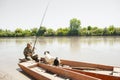 Focused male angler fiddling with tackle, while sitting with cute dog in shabby boat on shore. Royalty Free Stock Photo