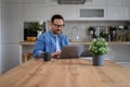 Focused male entrepreneur working over laptop on wooden desk in home office, with glasses Royalty Free Stock Photo