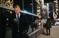 Focused male executive using a smart phone on a city street at night with festive light bokeh in the background. Royalty Free Stock Photo