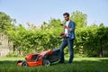 Focused male gardener using smartphone, while having break after trimming lawn in garden. Royalty Free Stock Photo