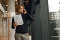 Focused male sales manager in eyeglasses is talking phone standing with documents in coworking space Royalty Free Stock Photo