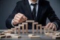 Focused man in black suit builds wooden block bridge on table, symbolizing strategy and planning