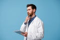 Focused man doctor in white coat stands with clipboard in hands and looks away Royalty Free Stock Photo