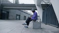 Focused man using smartphone outdoor. Young hipster sitting on skateboard.