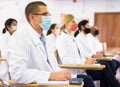 Focused man in white coat and protective mask attending medical seminar