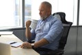 Focused mature businessman deep in thought while sitting at the desk with cup of coffee in his hand in modern office. Royalty Free Stock Photo