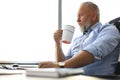 Focused mature businessman deep in thought while sitting at the desk with cup of coffee in his hand in modern office Royalty Free Stock Photo