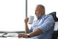 Focused mature businessman deep in thought while sitting at the desk with cup of coffee in his hand in modern office Royalty Free Stock Photo