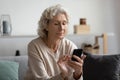 Focused mature woman using phone at home, looking at screen