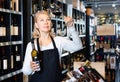 Focused mature woman wine producer inspecting quality of wine in wineshop on background with shelves of wine bottles