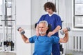 Osteopath correcting old man patients movements during rehabilitation with dumbbells