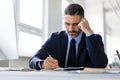 Focused middle aged businessman sitting at desk in office and writing in notepad, checking agenda Royalty Free Stock Photo