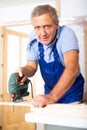 Concentrated male builder in uniform using a jigsaw machine on wooden plank at the apartment Royalty Free Stock Photo