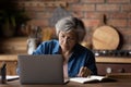 Focused middle aged woman in eyeglasses working remotely on computer.